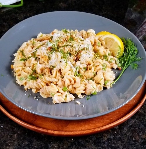 creamy tuna pasta on a grey plate with lemon wedges and fresh dill