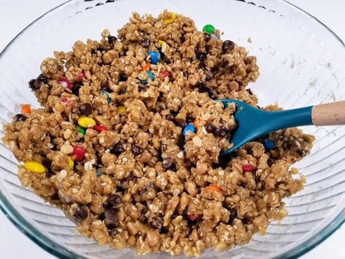 monster cookie bar ingredients mixed together in a bowl with spoon