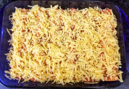 six unbaked chicken enchiladas rolled up in a baking dish covered with red sauce and shredded cheddar cheese