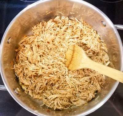 shredded chicken with taco seasoning in a pot on a black stove top