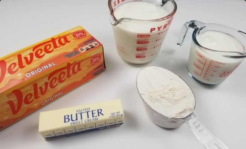 ingredients for cheese sauce, a box of velveeta cheese, stick of butter, 3/4 cup of flour and 3 cups of milk on a white counter