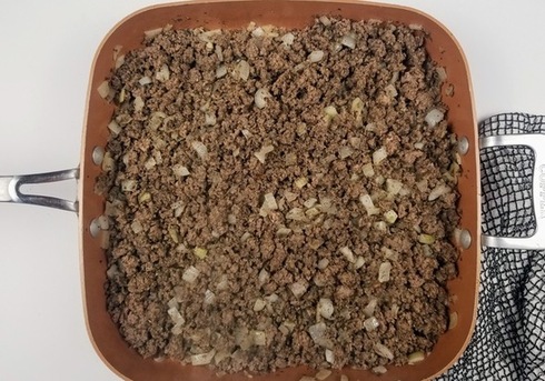 cooked hamburger and onions in a pan on a white counter