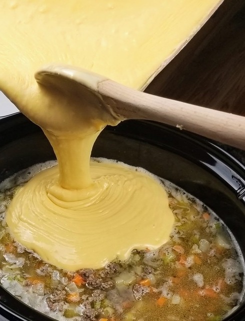 cheese sauce being poured into cheeseburger soup broth