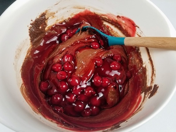cherries being folded into chocolate cake mix in a bowl