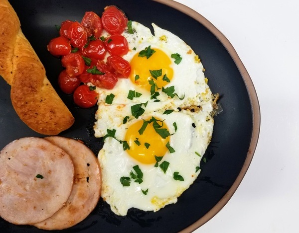 eggs, tomatos, garlic bread and Canadian bacon on a black plate